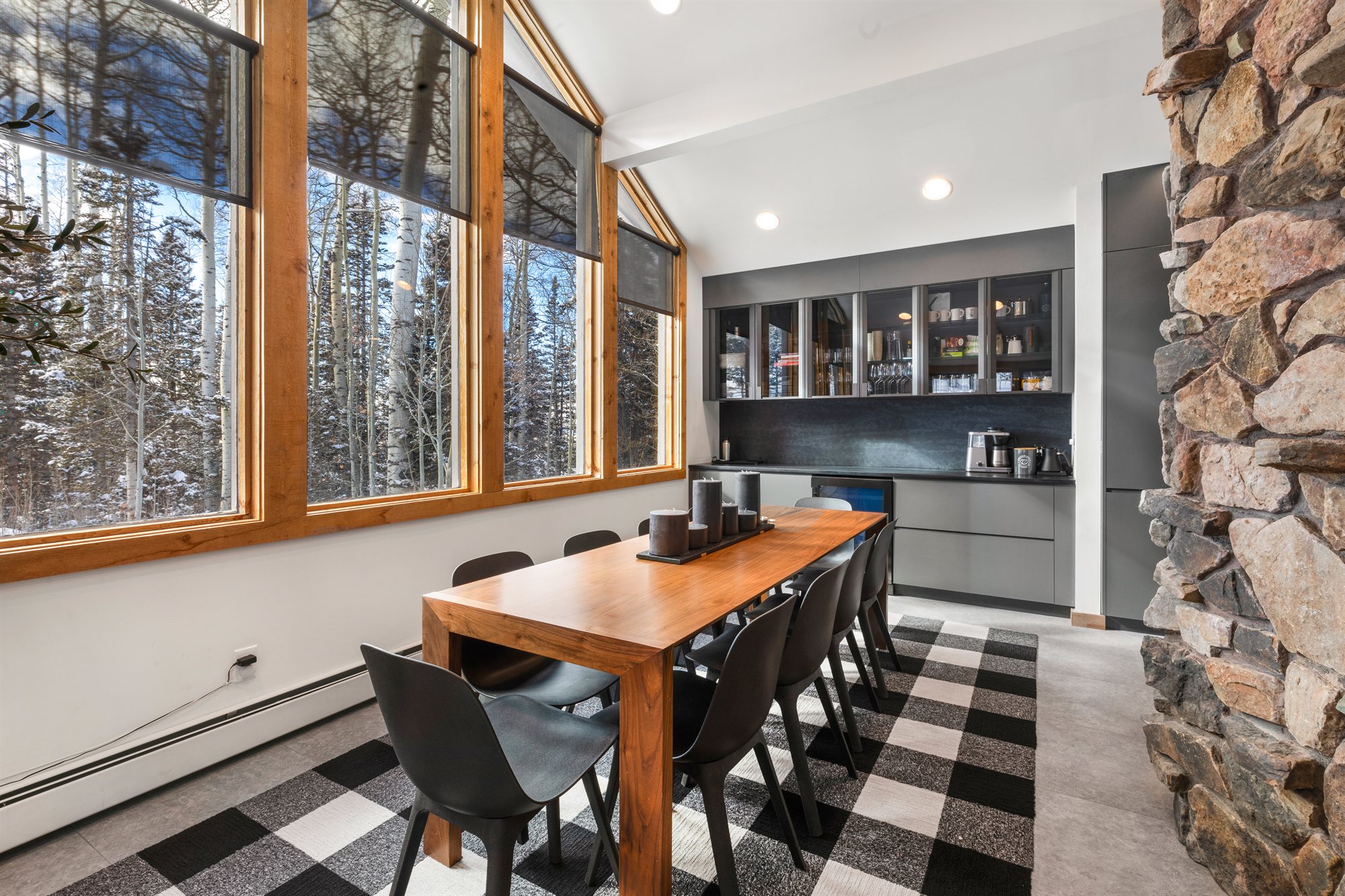 Dining table facing the buffet and wet bar, framed by tall forest-view windows