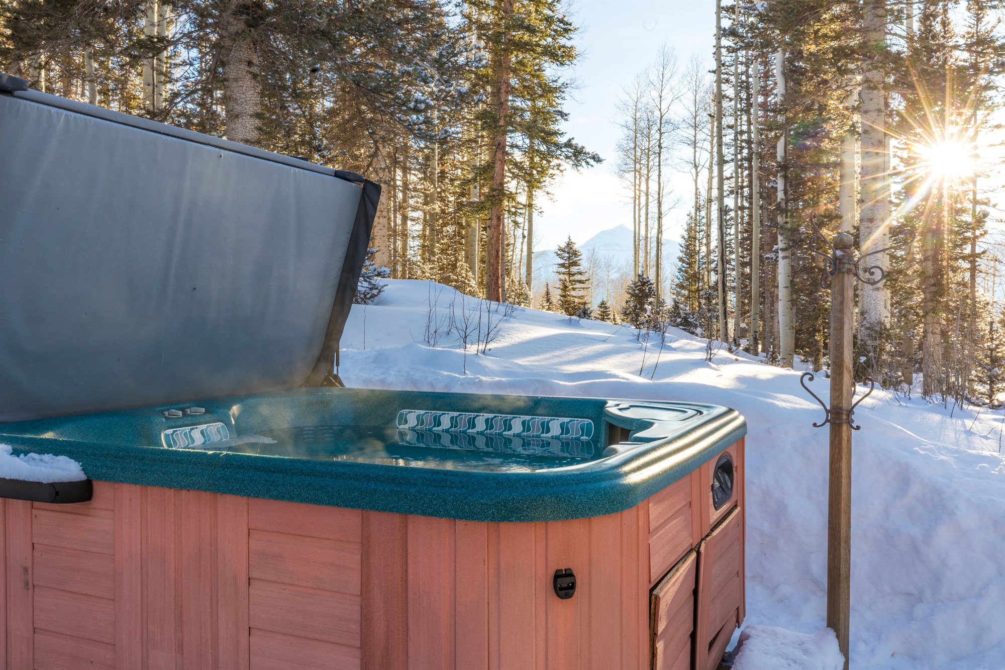 Steaming hot tub in the snow with late sun through the pines and a peak beyond