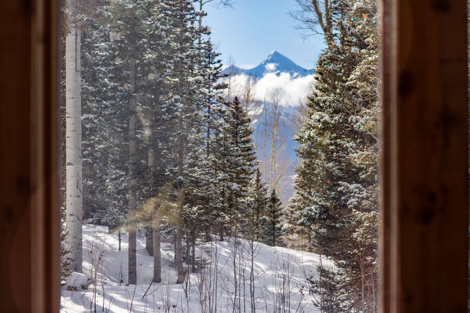 Snow-laden pines and alpenglow on the peak, framed by a lodge window